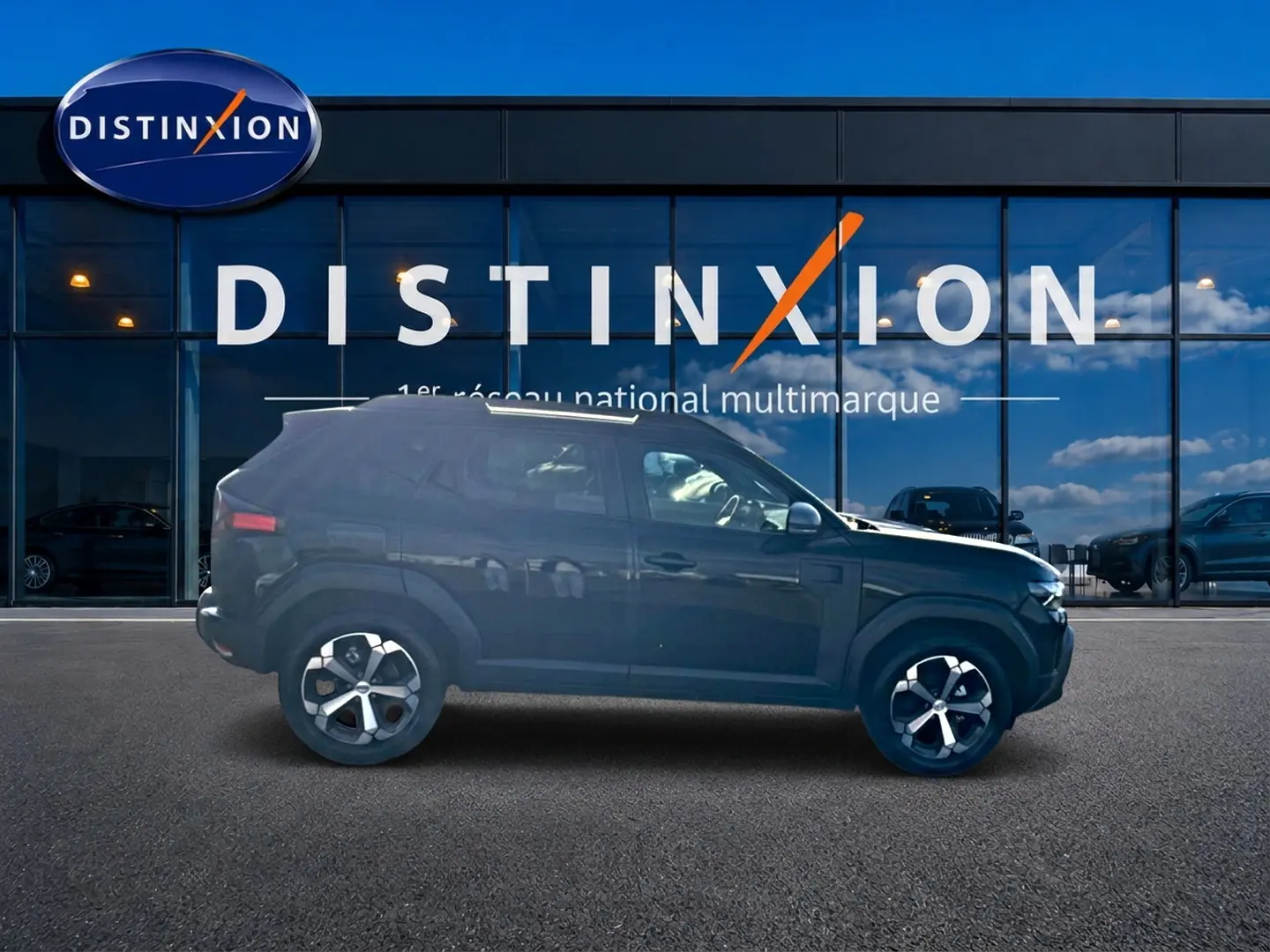 Vue de profil côté gauche d'un Dacia Duster noir 2026 garé devant une vitrine avec logo Distinxion.