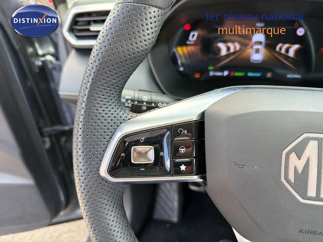 Gros plan sur le volant perforé gris du MG ZS 1.5L Hybrid+ 2025, avec commandes intégrées et tableau de bord numérique en arrière-plan.