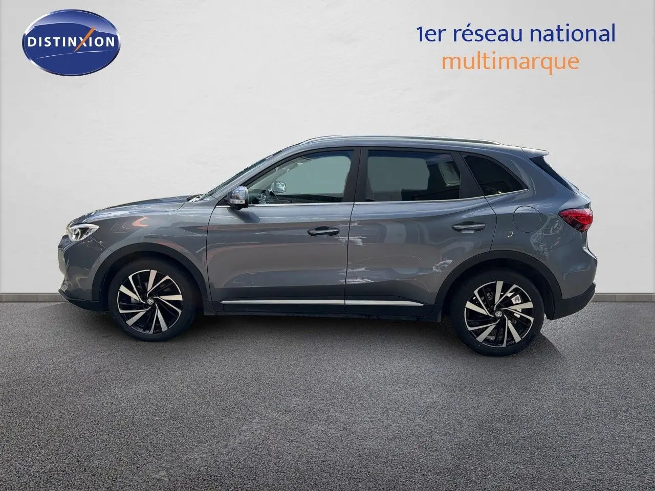 Vue de profil côté gauche du MG MOTOR ZS 1.5L HYBRID+ 197CH LUXURY 2025 en gris Hampstead avec jantes alliage bicolores.