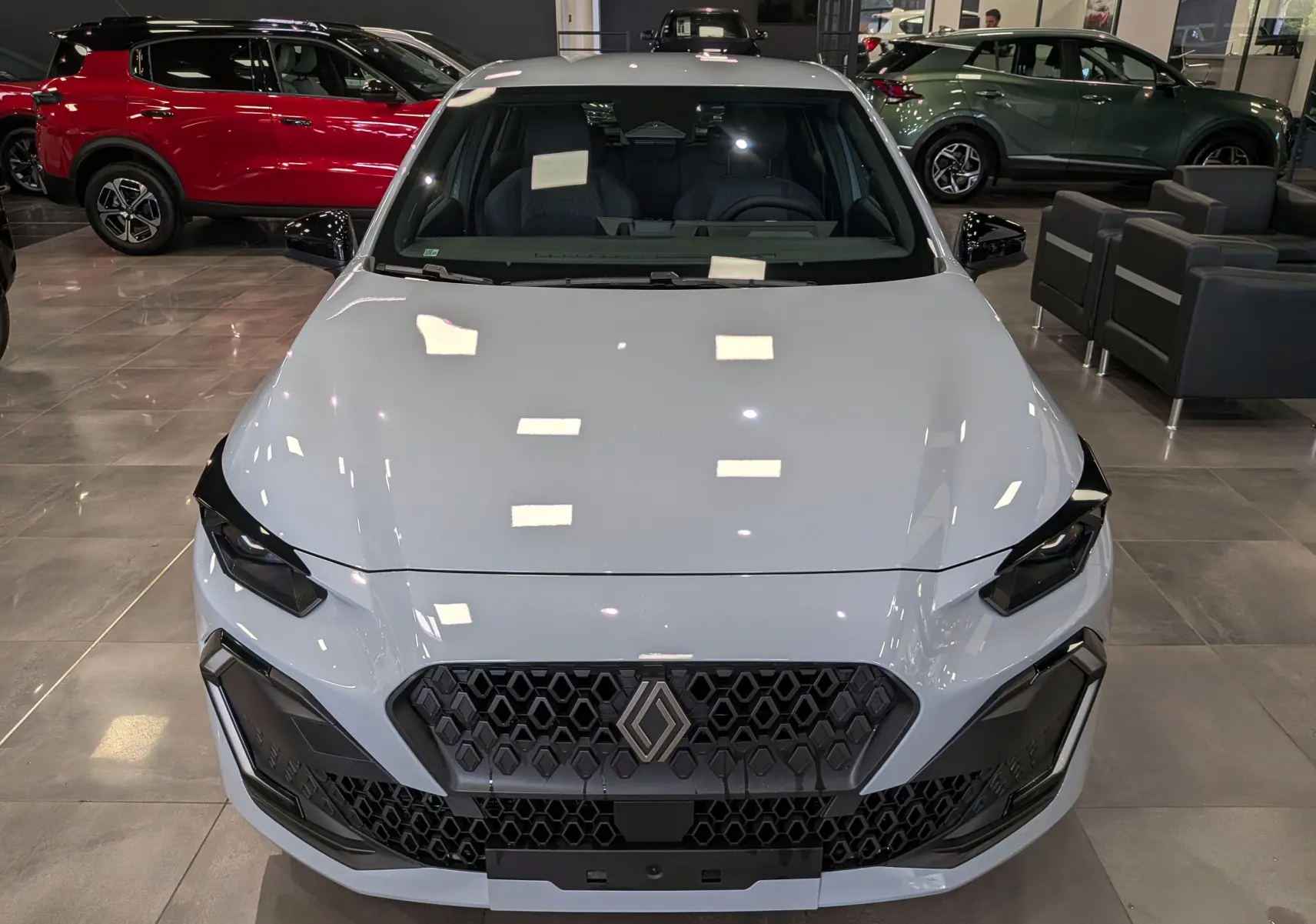 Vue avant de la Renault Clio VI 1.2 TCe 115 Gris Rafale en showroom, soulignant sa calandre hexagonale et ses phares anguleux.