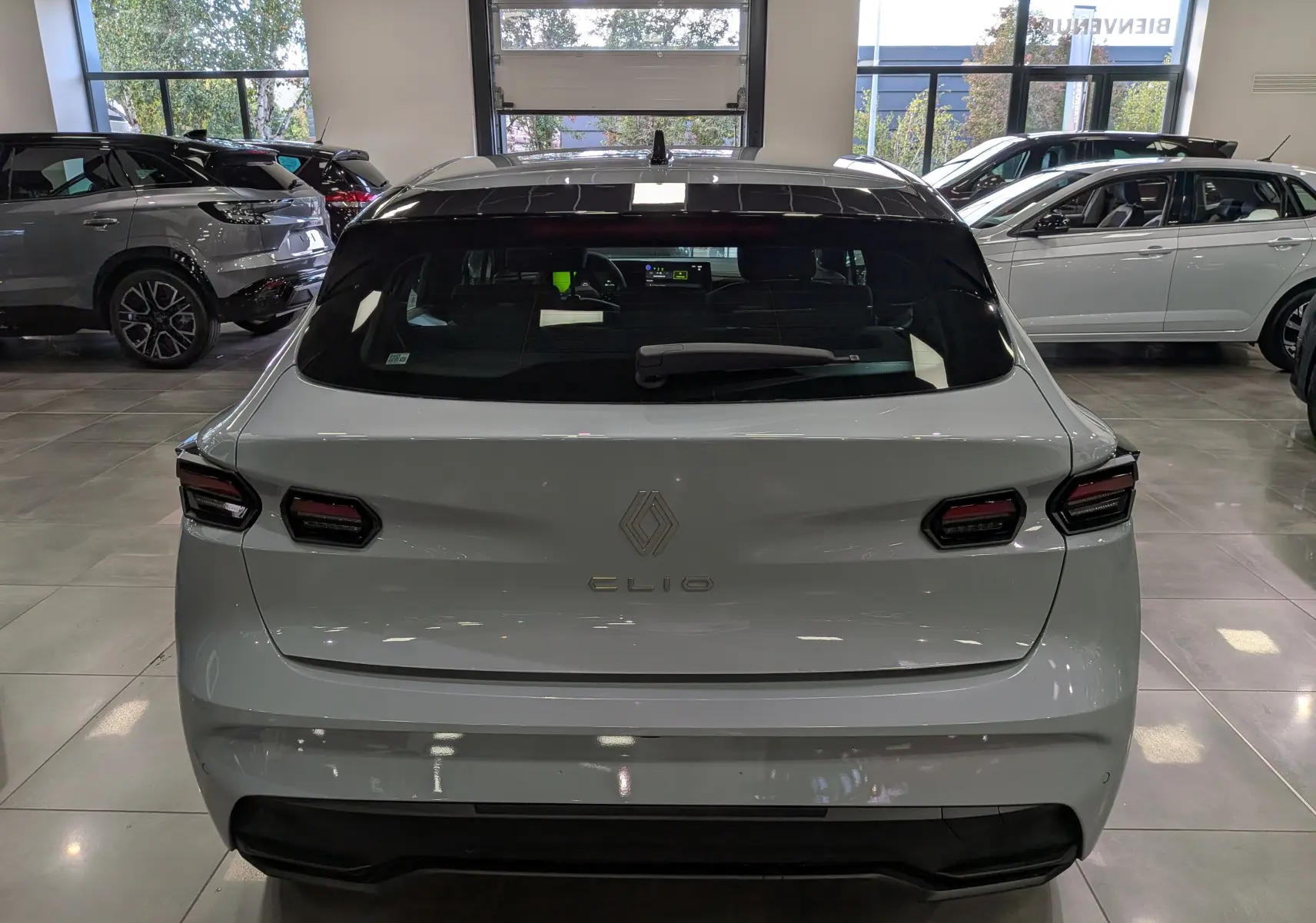 Vue arrière d'une Renault Clio VI gris Rafale, mettant en valeur ses feux arrière LED et le logo central sur le hayon.