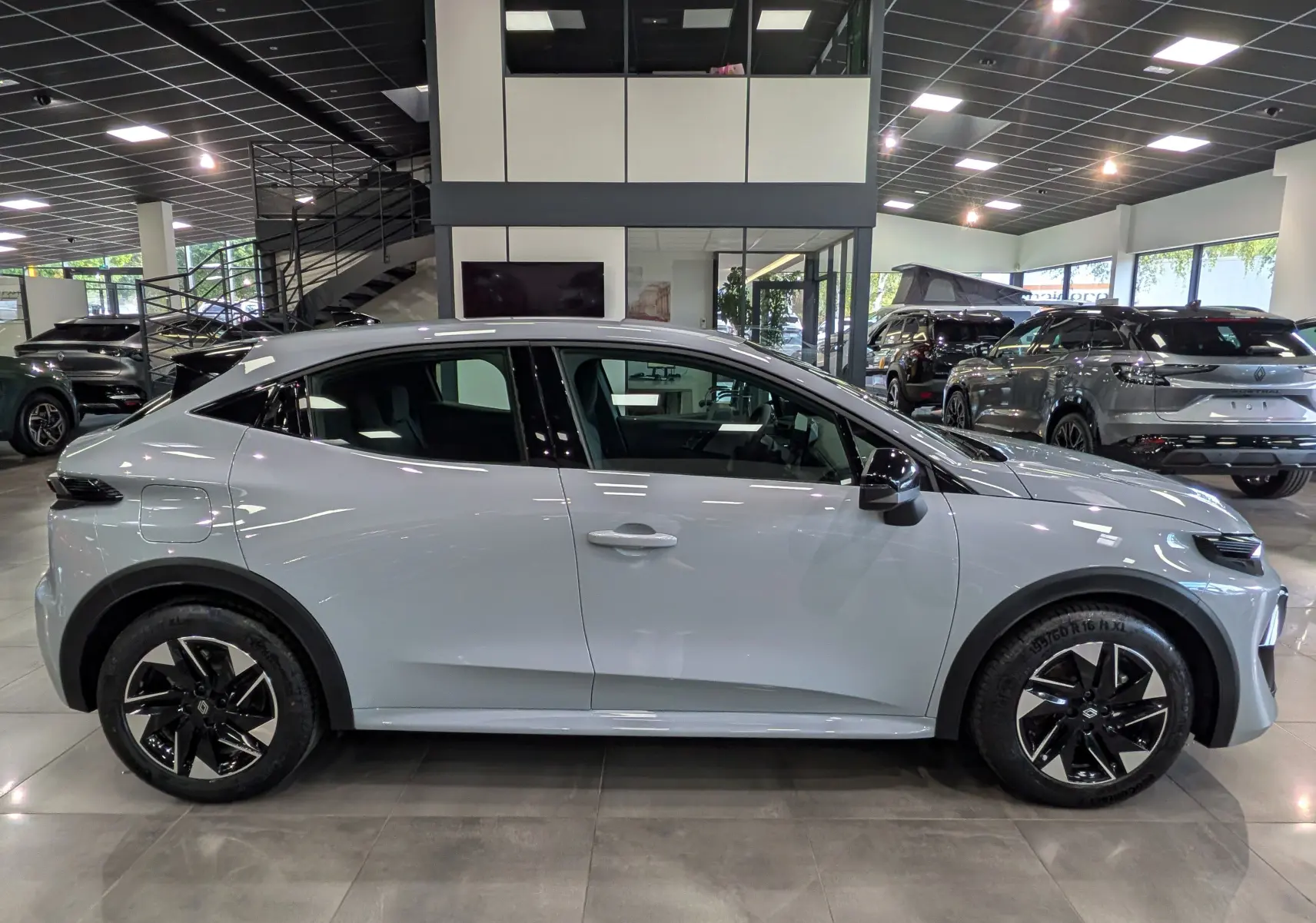 Profil côté gauche de la Renault Clio VI gris Rafale 2026 en showroom, avec jantes noires bicolores et lignes fluides.