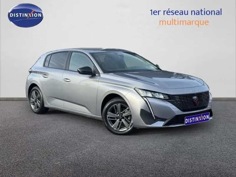 Peugeot 308 Gris Artense vue 3/4 avant droit, avec calandre noire distinctive et jantes alliage.