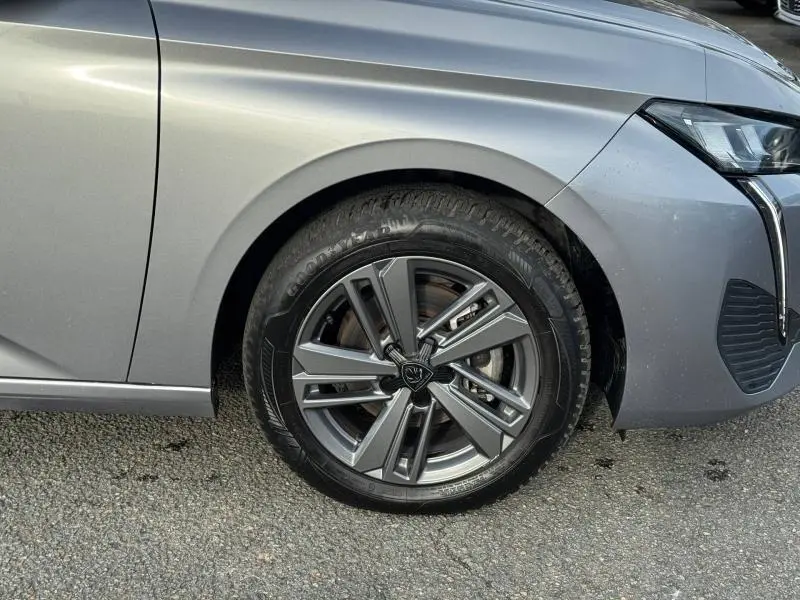 Gros plan sur la roue avant droite et l’aile d’une Peugeot 308 1.2 PureTech gris Artense 2024, avec jante alliage distinctive.