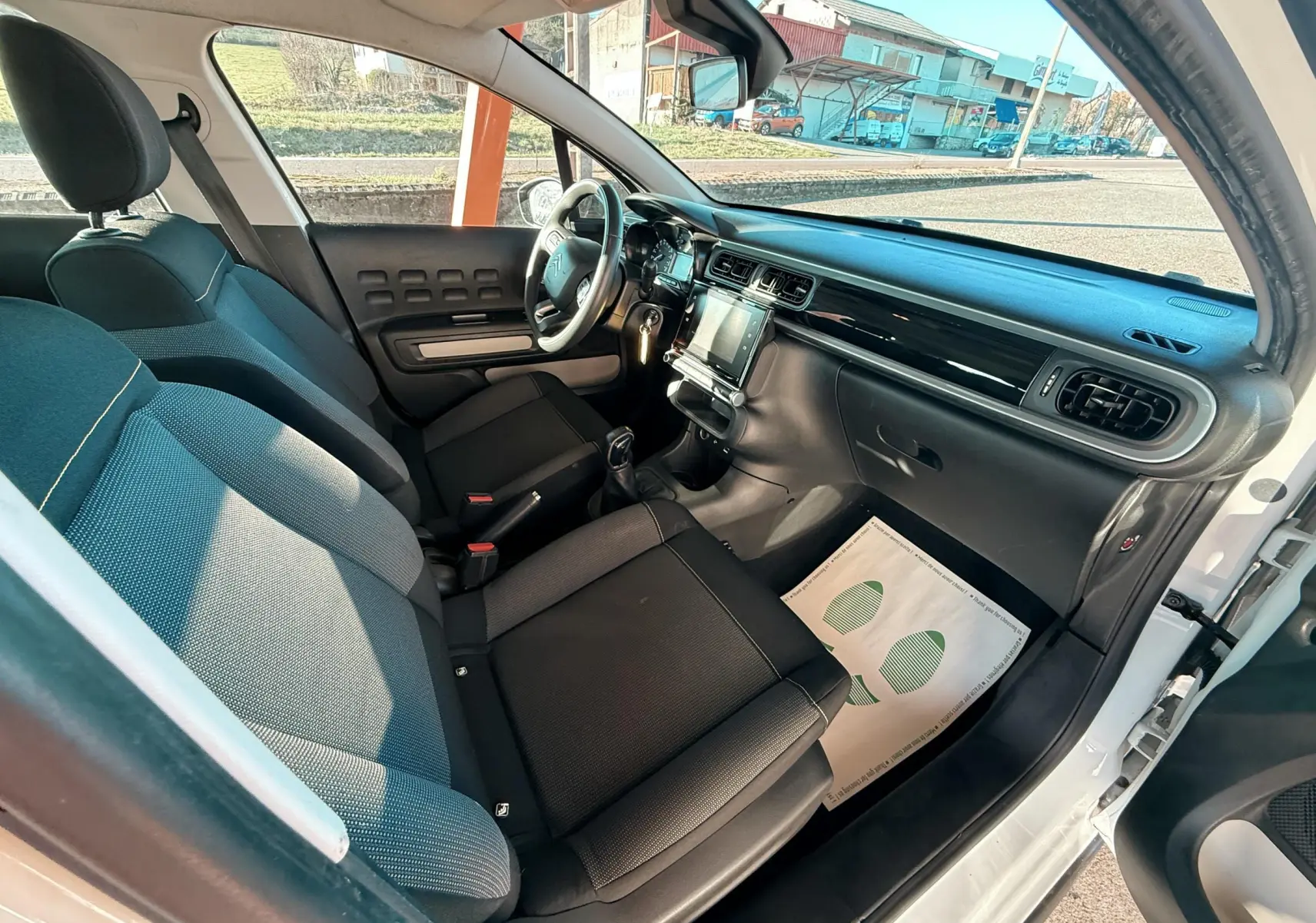 Vue intérieure côté conducteur de la Citroën C3 blanche 2017, sièges tissu gris noir et tableau de bord moderne.