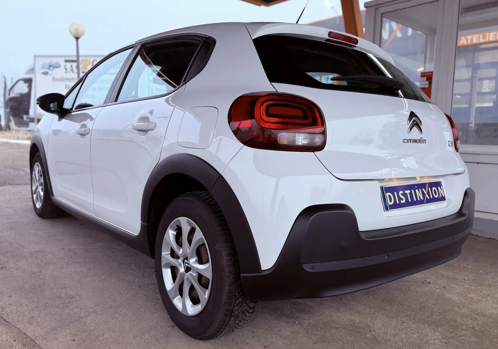 Vue 3/4 arrière droite d'une Citroën C3 blanche avec feux arrière distinctifs et protections noires sur les ailes.