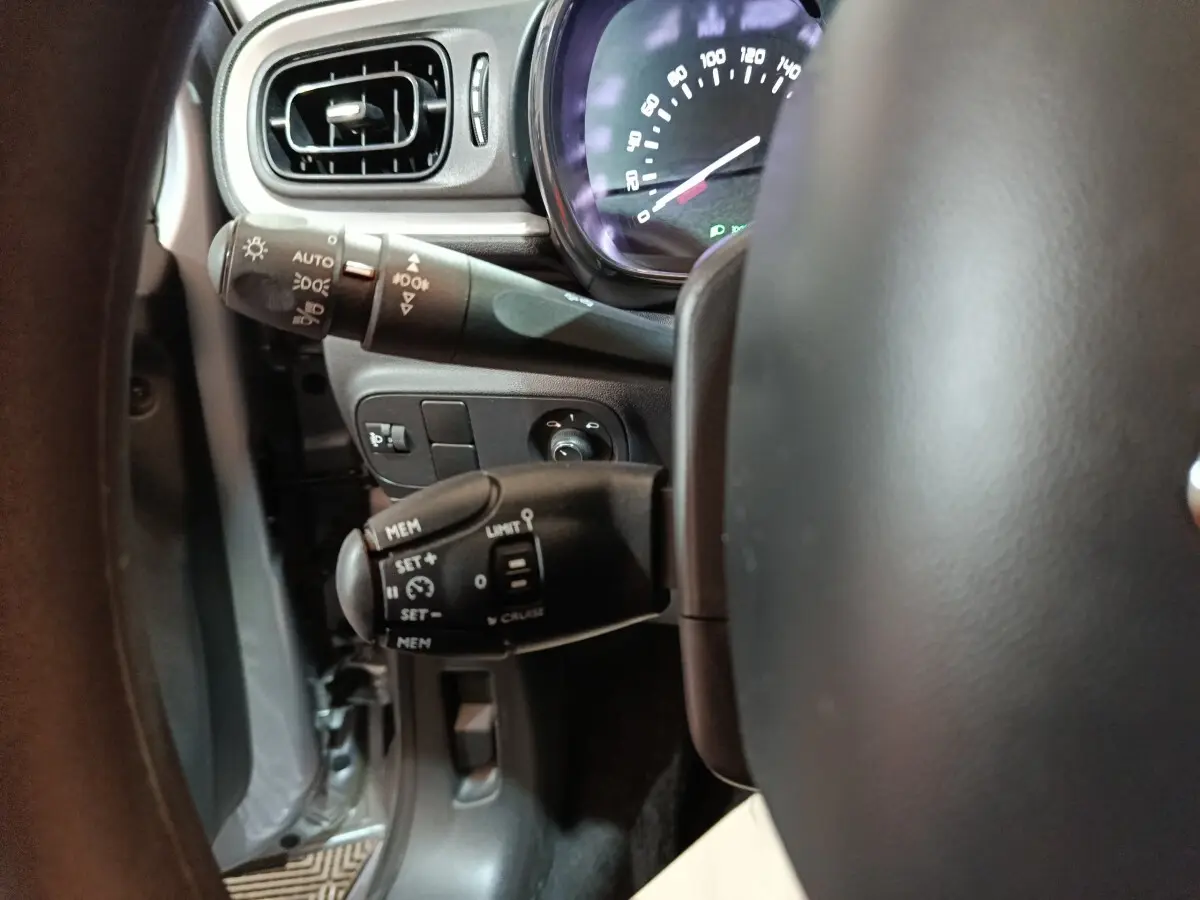 Gros plan sur la partie gauche du volant d'une Citroën C3 gris clair 2024, montrant commandes de régulateur et tableau de bord.