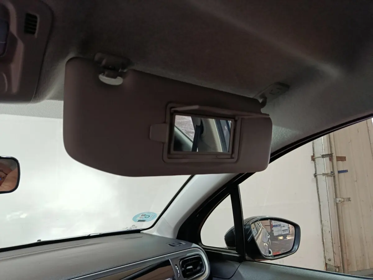 Vue intérieure côté conducteur du pare-soleil avec miroir intégré et rétroviseur extérieur noir d'une Citroën C3 gris clair.