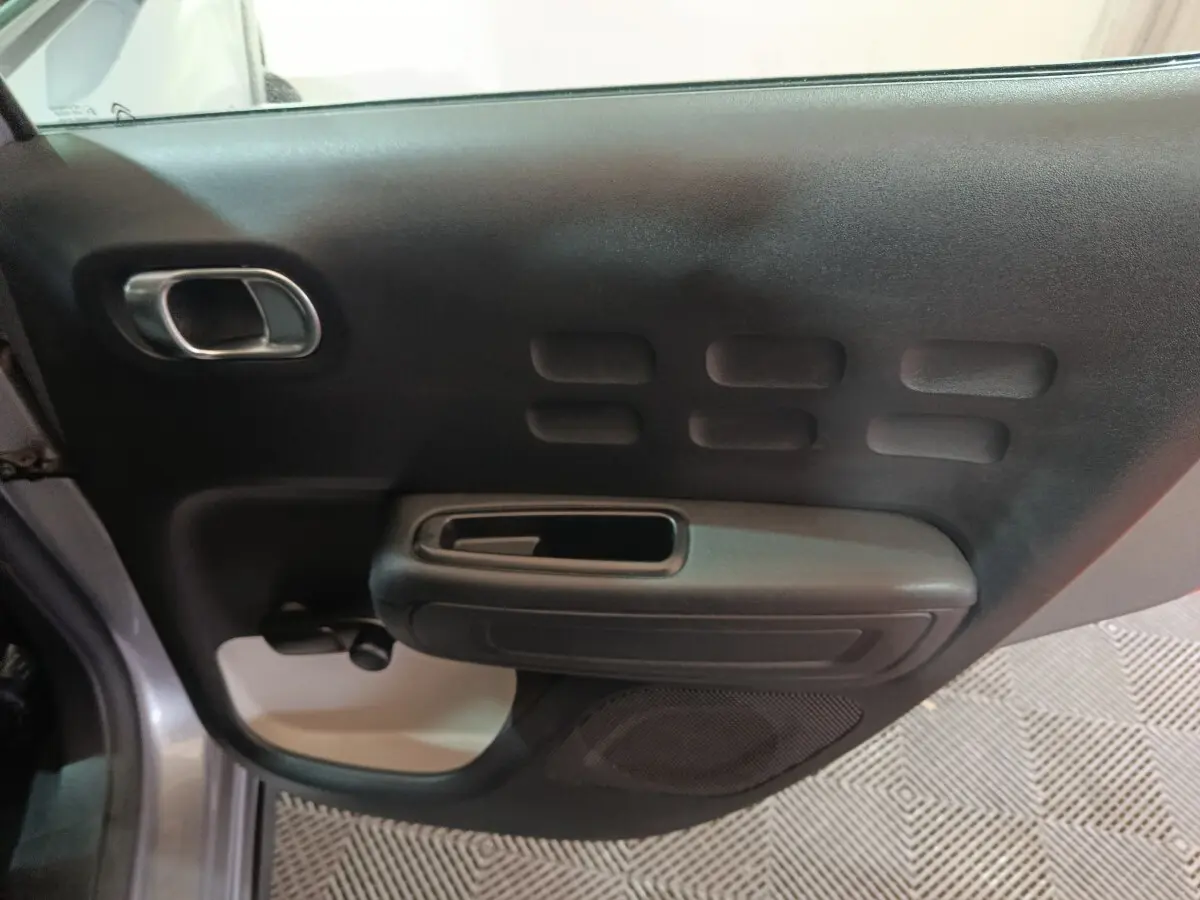 Vue intérieure côté gauche de la porte avant gris clair de la Citroën C3 avec poignée et haut-parleur intégrés.