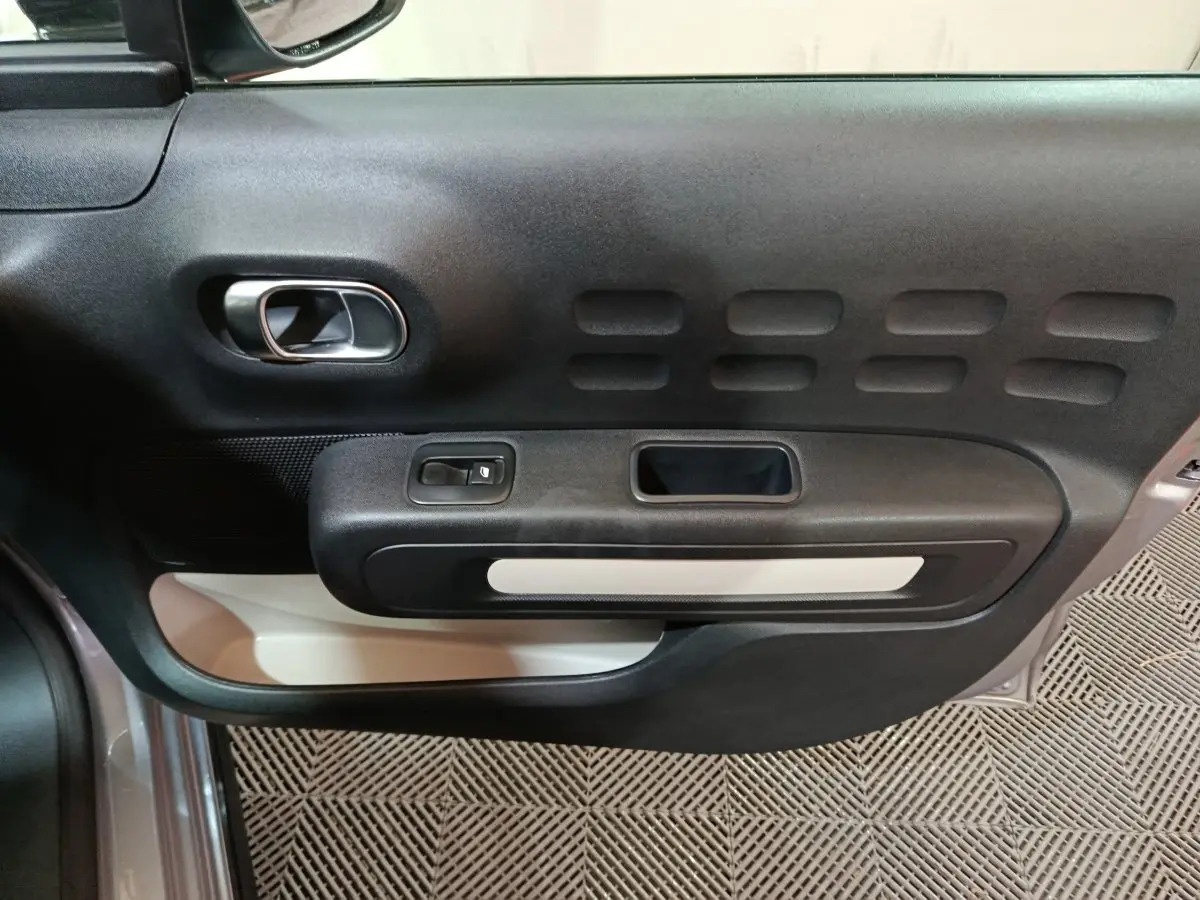 Vue rapprochée de la porte côté conducteur de la Citroën C3 gris clair, montrant la poignée intérieure et les commandes de fenêtre.