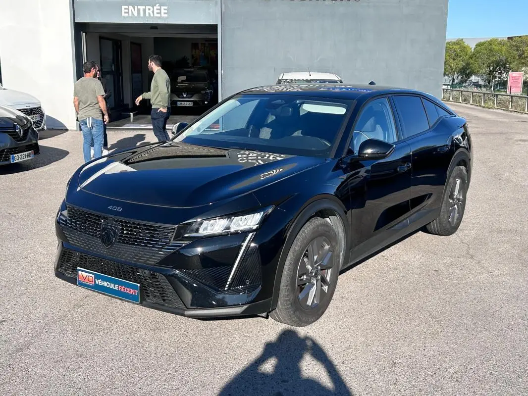 Peugeot 408 PHEV noir vue 3/4 avant droit, jantes alliage 17 pouces, stationnée devant un bâtiment avec entrée visible.
