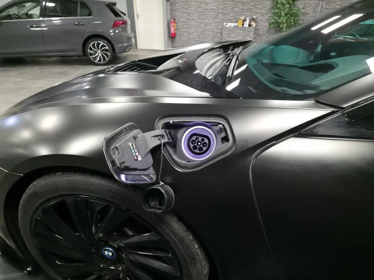 Prise de recharge ouverte côté gauche sur BMW i8 Coupé Pure Impulse noir mat, avec jante noire profilée 20 pouces visible.
