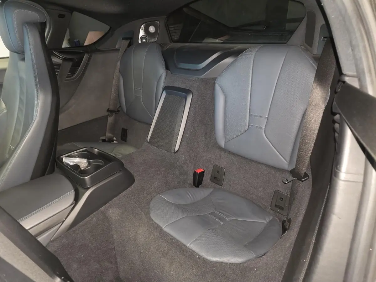 Vue intérieure arrière droite de la BMW i8 noire, montrant les sièges arrière en cuir perforé et la console centrale avec porte-gobelets.