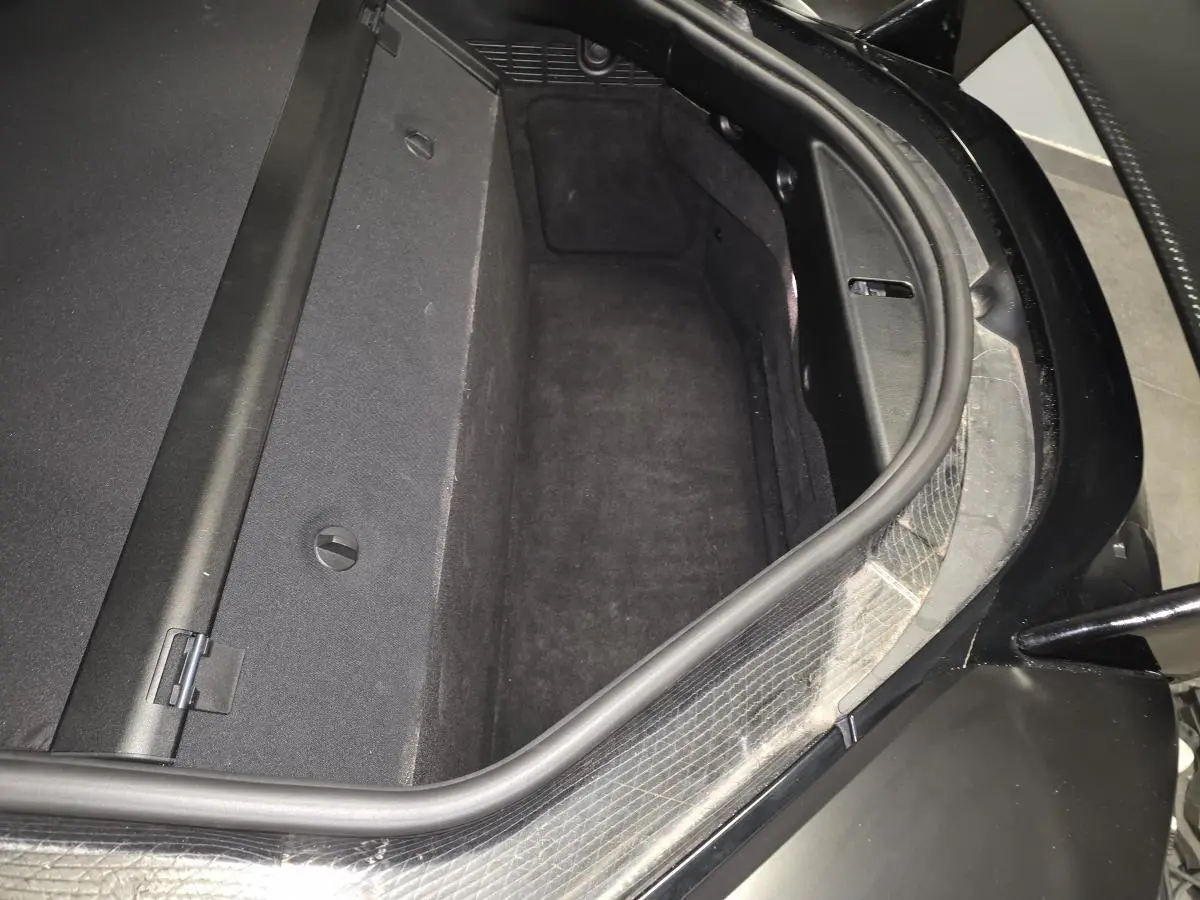 Coffre arrière ouvert vu de dessus sur BMW i8 noir mat, montrant l'espace de rangement et les finitions intérieures.