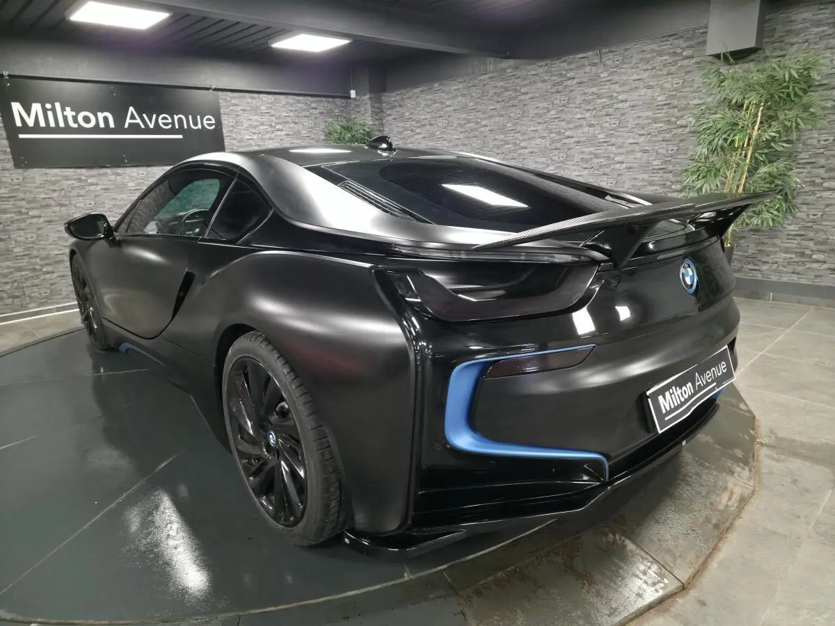 BMW i8 Coupé Pure Impulse noir mat vue 3/4 arrière droit avec aileron carbone et détails bleus lumineux.