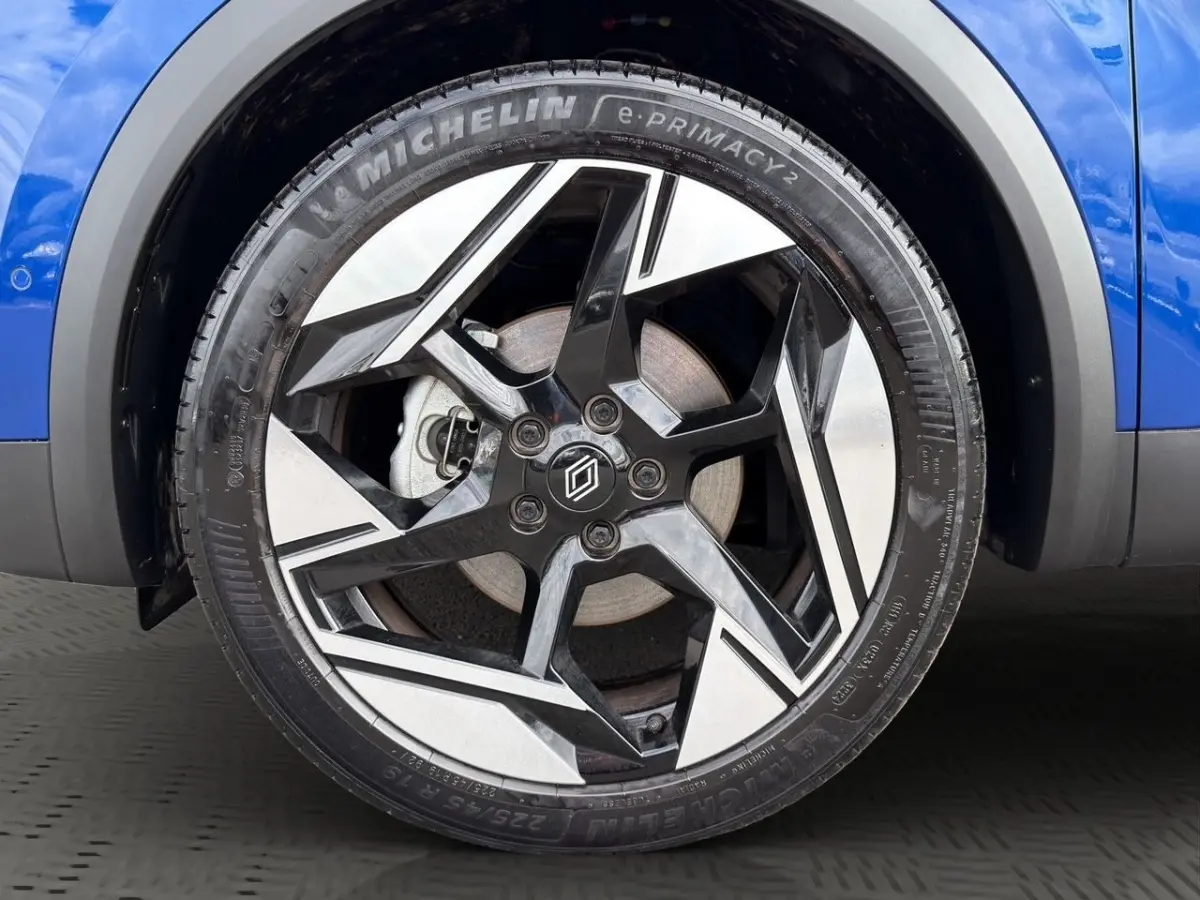 Gros plan sur la roue avant droite bleu Renault Symbioz avec jante noire et argentée au design géométrique.