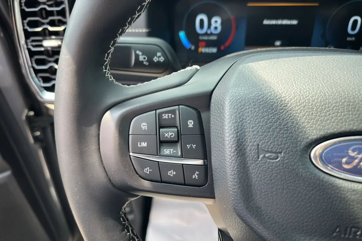 Gros plan sur le volant cuir multifonctions du Ford Ranger gris carbone, avec commandes de régulateur et assistance visibles.