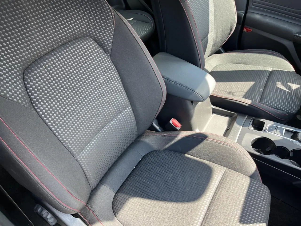 Gros plan sur les sièges avant noirs avec surpiqûres rouges et accoudoir central dans l’habitacle d’une Ford Focus SW bleue.