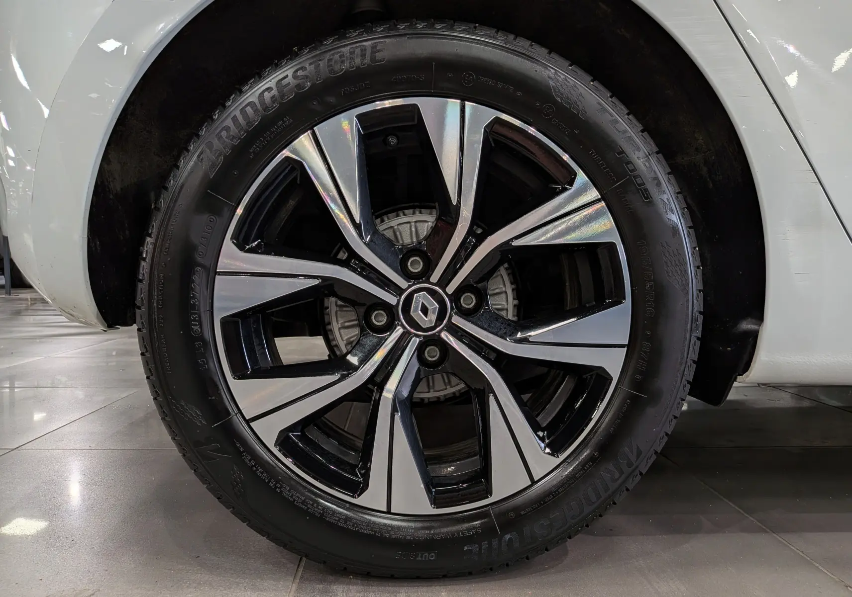 Gros plan sur la roue avant droite d’une Renault Clio V blanc glacier, jante alliage bicolore au design moderne.