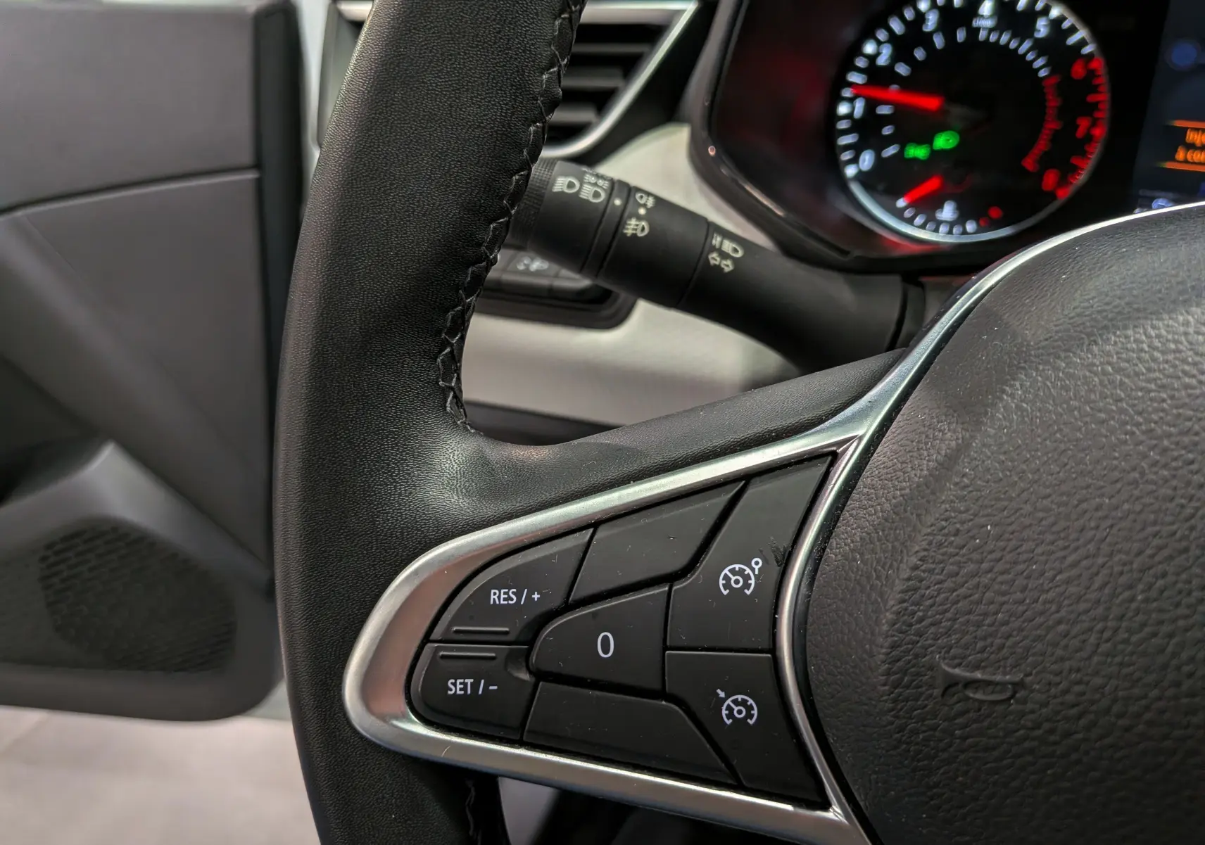 Gros plan sur le volant noir de la Renault Clio V 2022, montrant les commandes de régulateur de vitesse côté gauche.