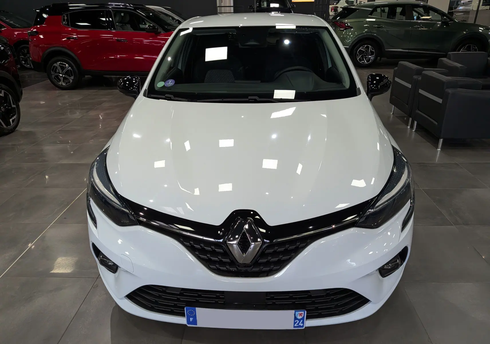 Vue avant d'une Renault Clio V blanche Glacier, mettant en valeur la calandre noire et les phares effilés dans un showroom.