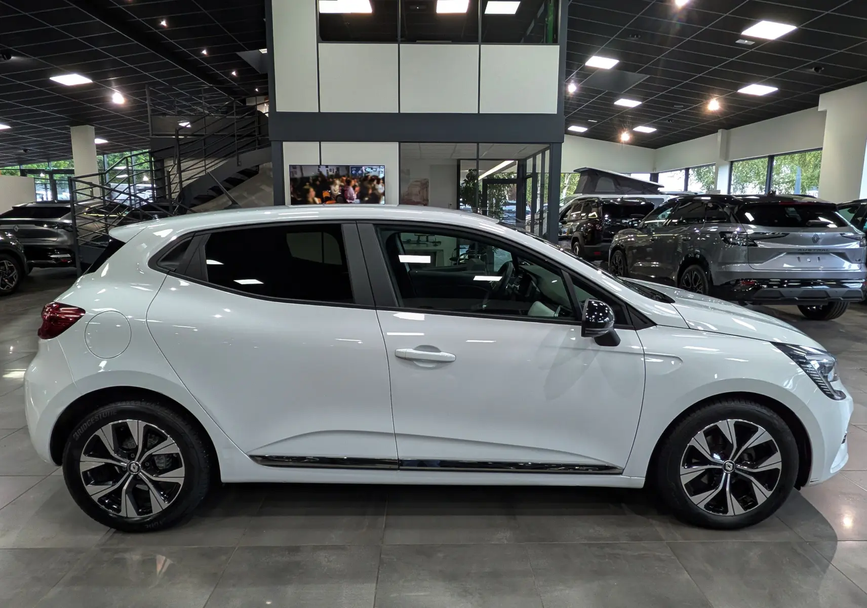 Profil droit de la Renault Clio V blanc glacier, version TCe 100 CH EVOLUTION GPL, en showroom lumineux.