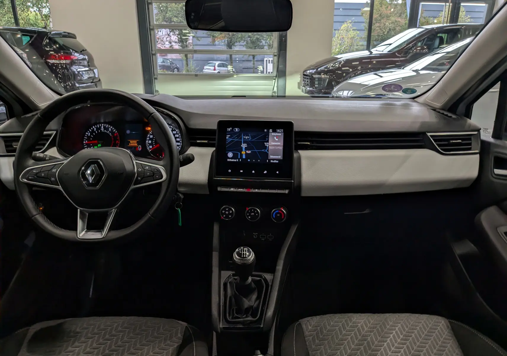 Vue intérieure avant de la Renault Clio V blanche, tableau de bord avec écran tactile et volant multifonction.