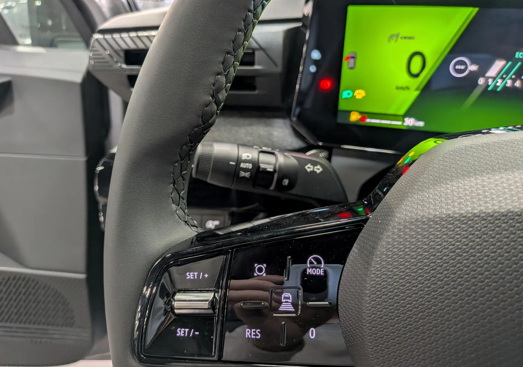 Gros plan sur le volant et la commande de régulateur de vitesse d'une Renault Clio VI gris schiste, avec tableau de bord numérique vert.