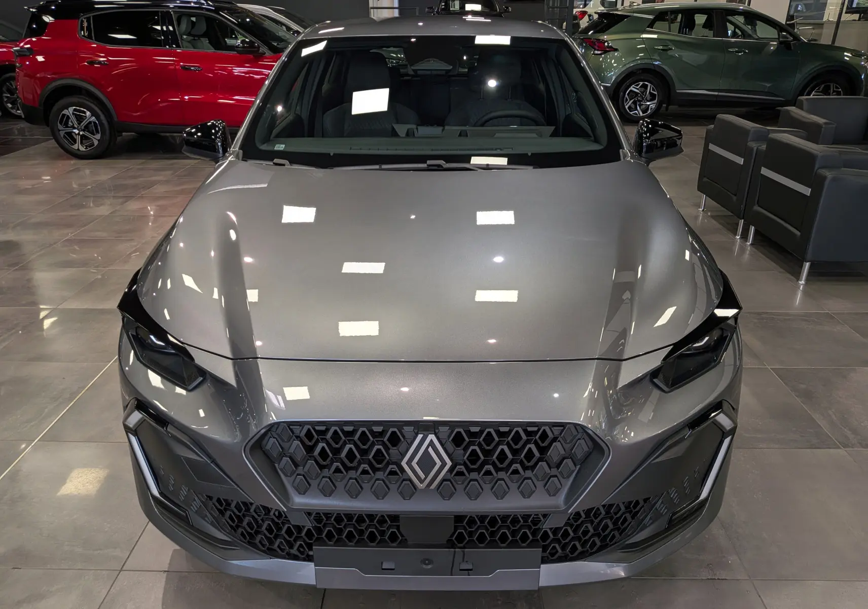 Vue avant plongeante d'une Renault Clio VI gris schiste, mettant en valeur sa calandre hexagonale et ses optiques anguleuses.