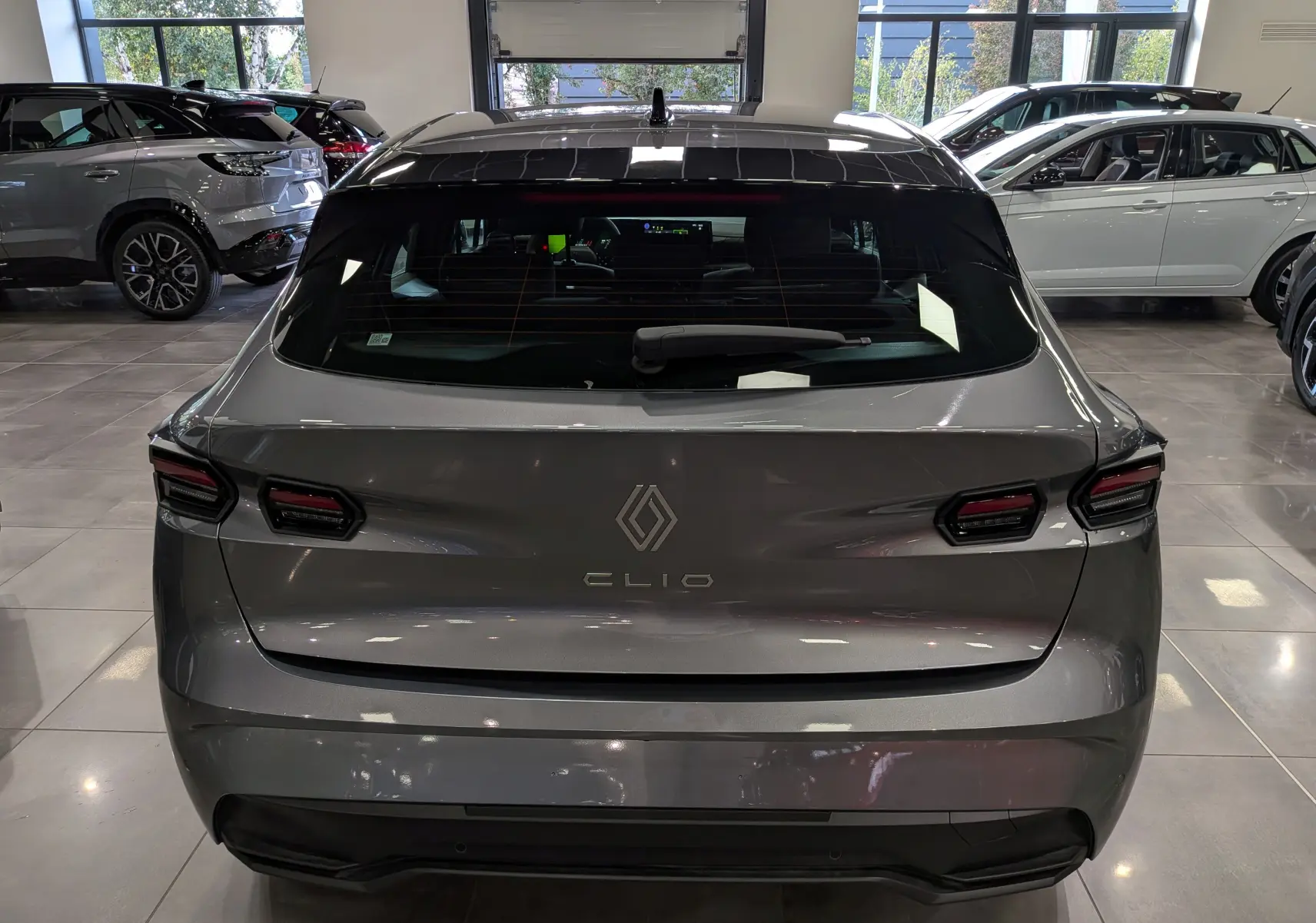 Vue arrière d'une Renault Clio VI gris schiste, avec feux arrière LED et lunette arrière teintée en showroom.