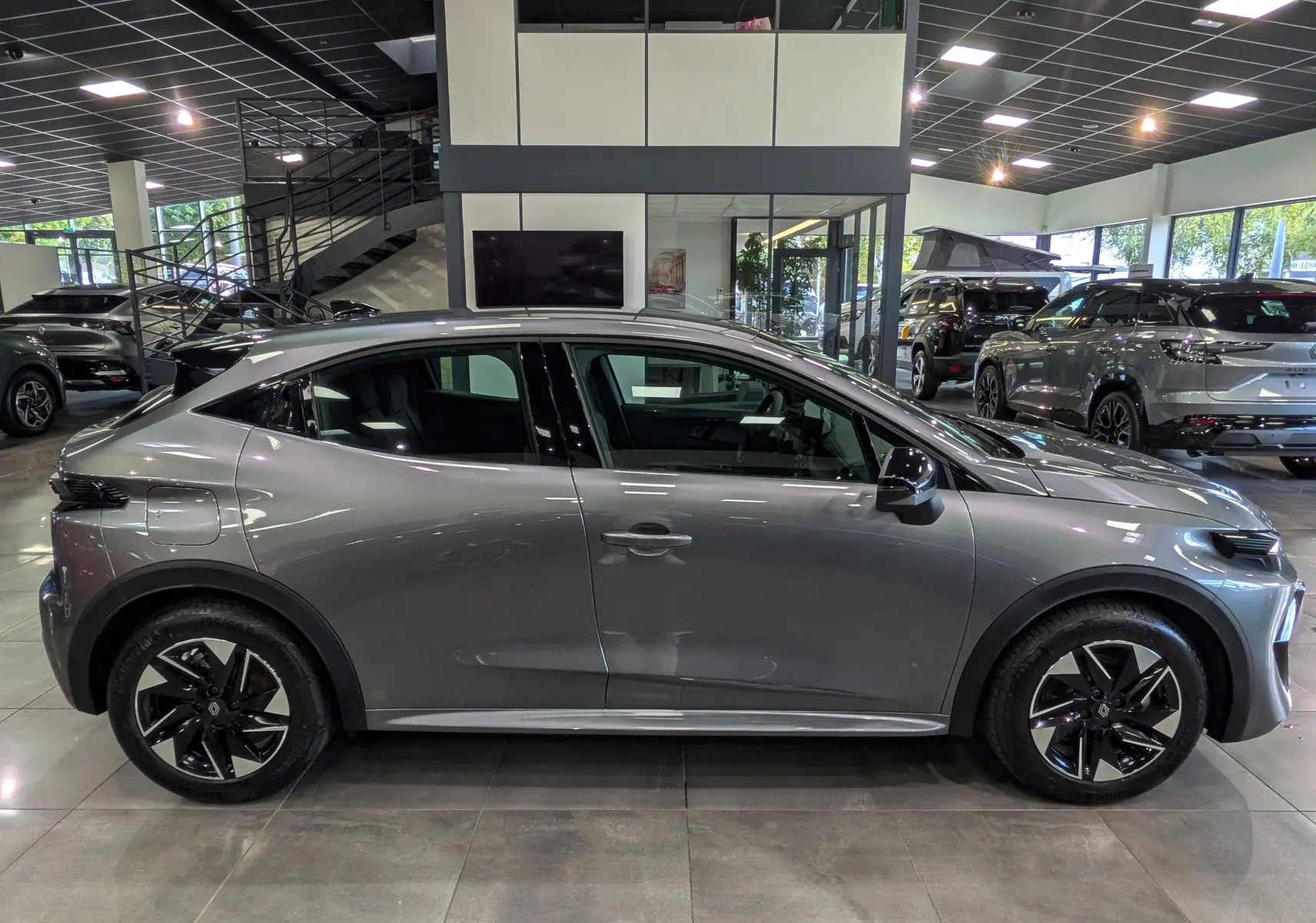 Profil droit d'une Renault Clio VI gris schiste 2026 en concession, avec jantes noires bicolores et lignes fluides.