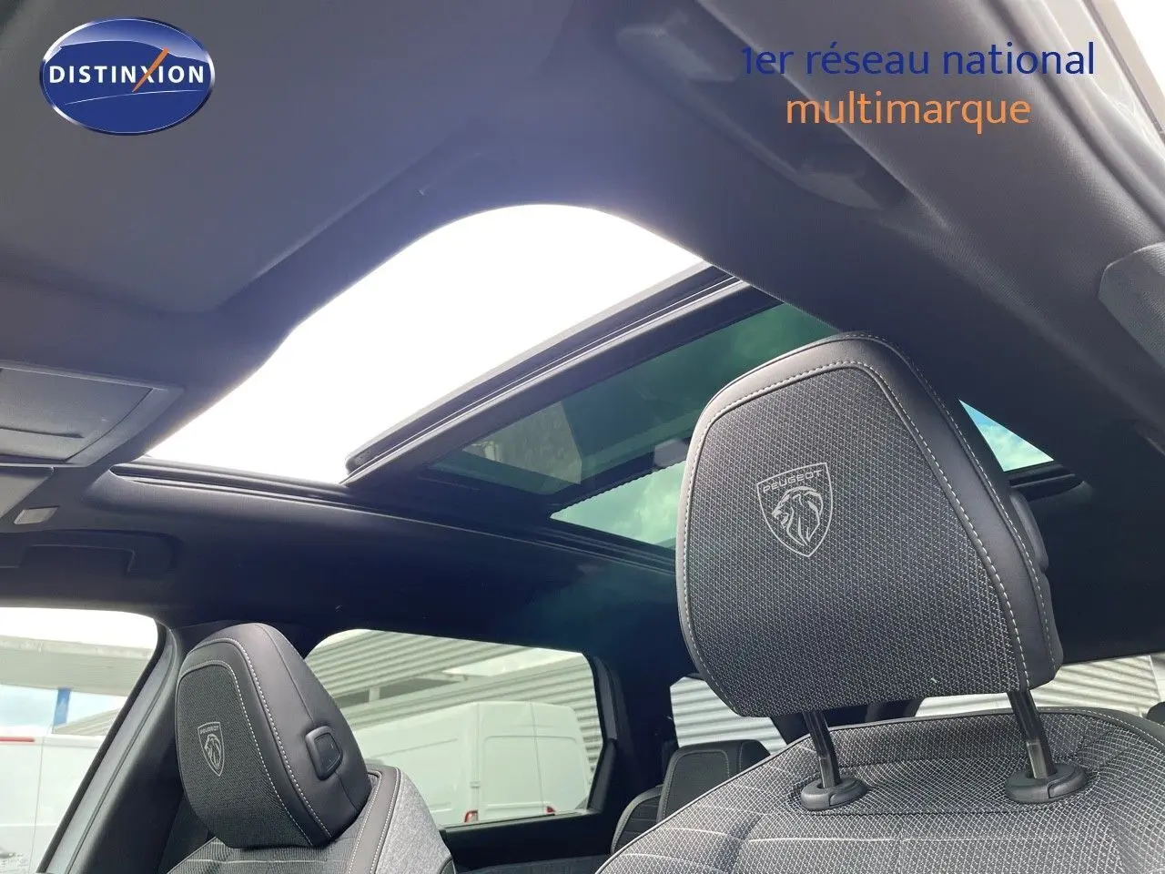 Vue intérieure du Peugeot 5008 Hybrid 2025 montrant les sièges avant en cuir noir avec logo Peugeot et toit panoramique ouvert.