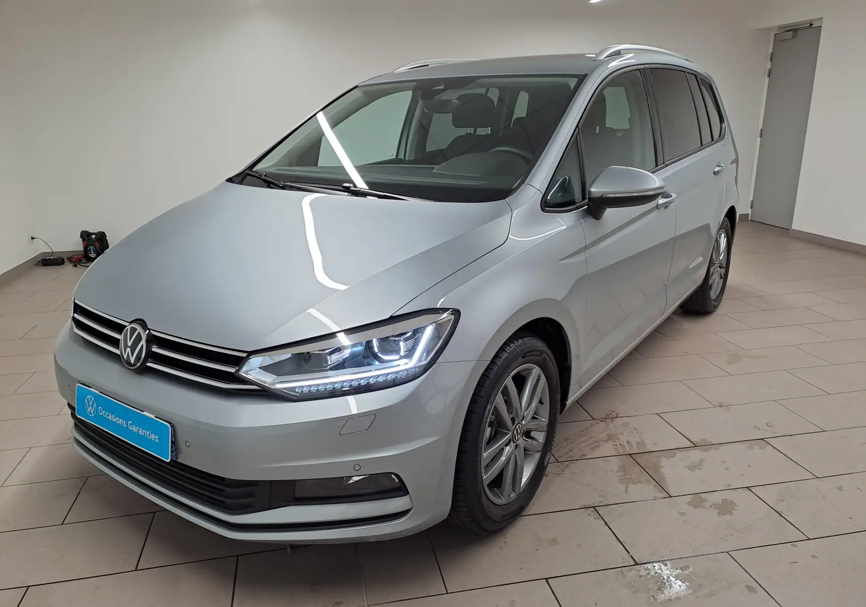 Volkswagen Touran 2025 argent Dolomite en 3/4 avant droit, avec feux LED et jantes alliage visibles.