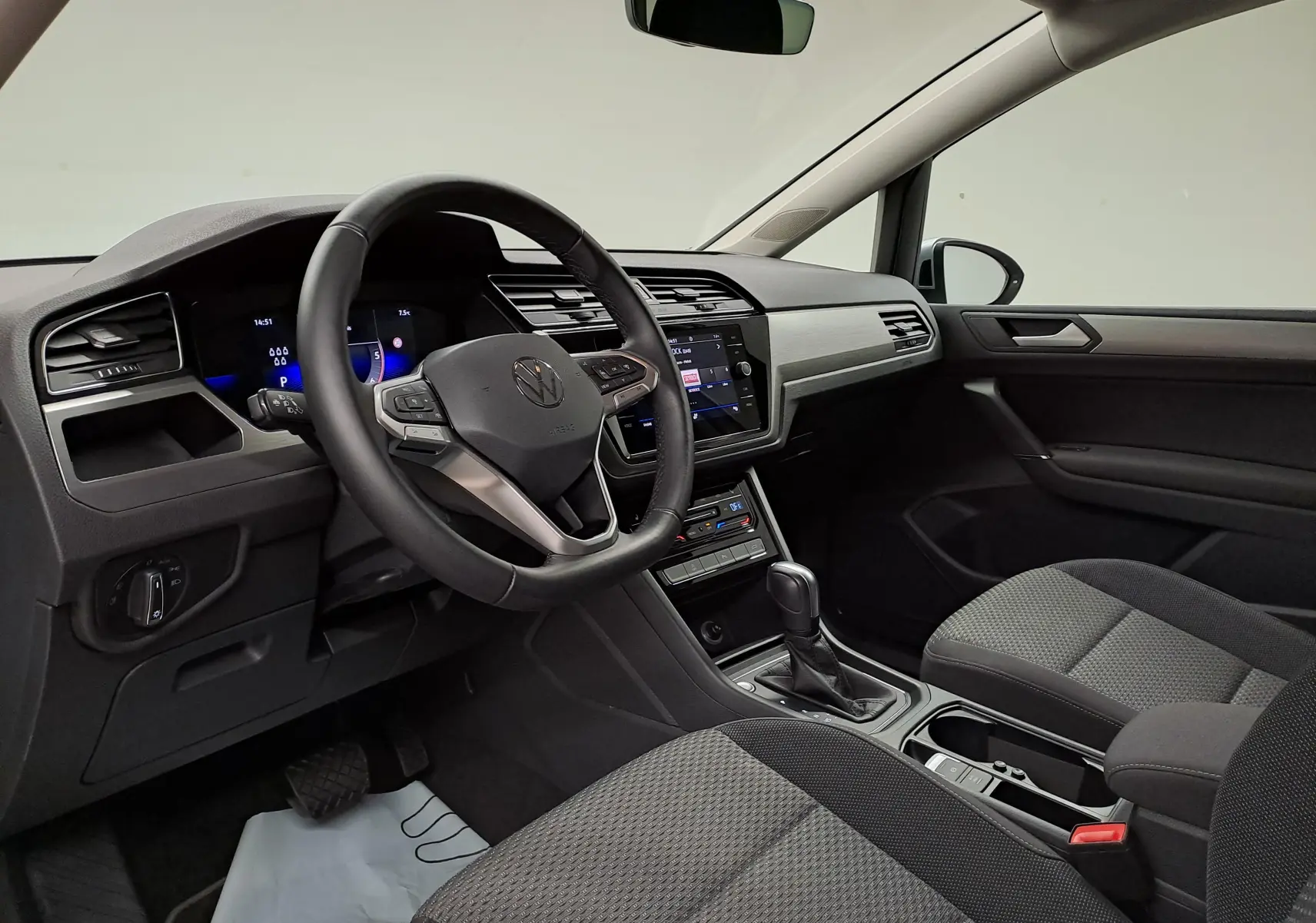 Vue intérieure côté conducteur du Volkswagen Touran 2025, tableau de bord moderne avec volant multifonction et sellerie tissu gris.