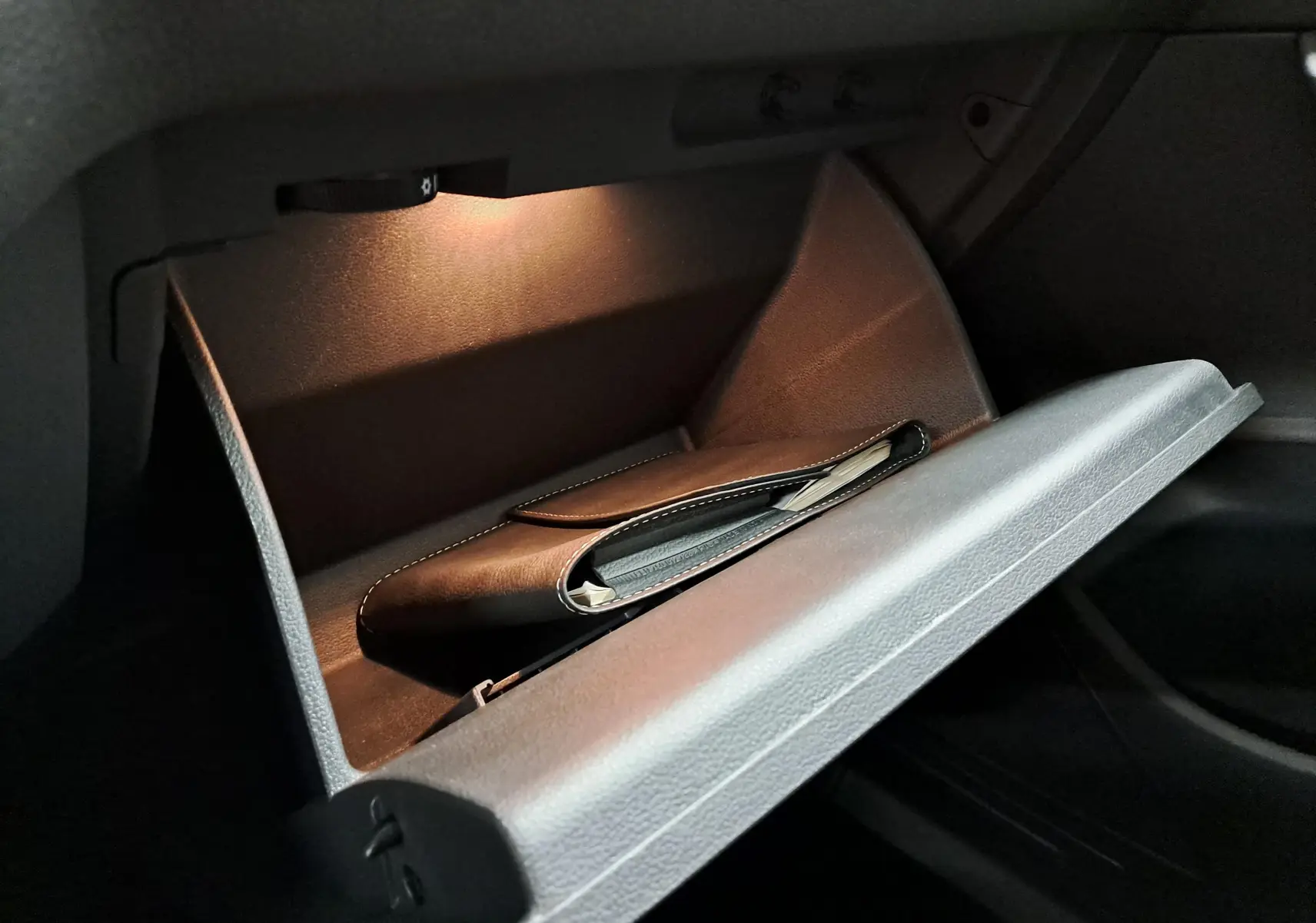 Gant de boîte à gants ouvert éclairé dans un Volkswagen Touran 2025, avec un étui noir à l'intérieur.