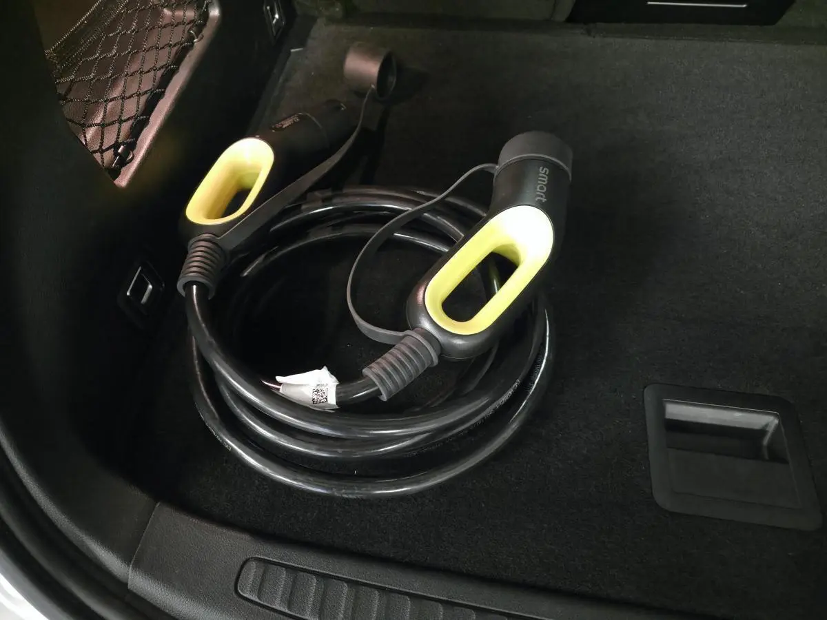 Câble de recharge électrique noir avec poignées jaunes dans le coffre d'une Smart Electric blanche, vue intérieure.