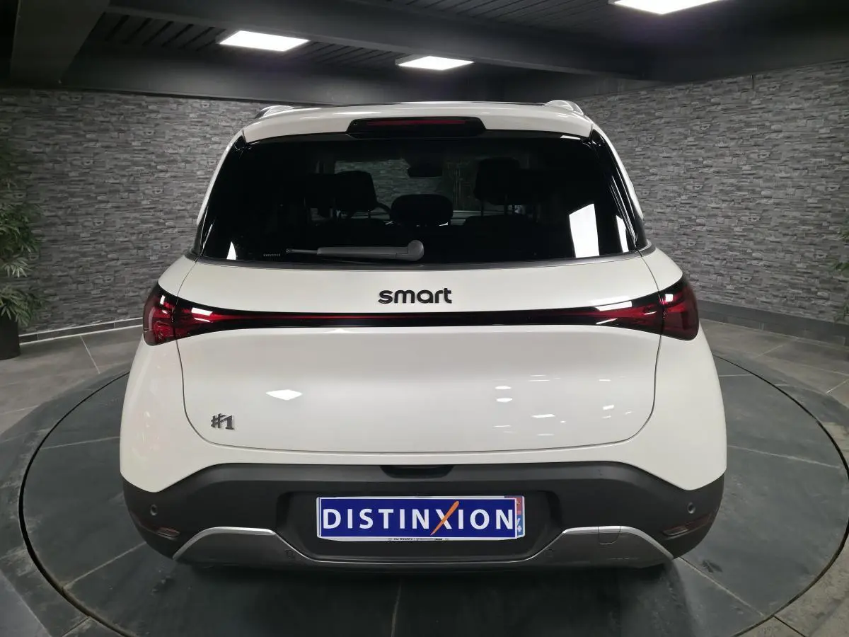 Vue arrière d'une Smart #1 électrique blanche 2024 avec feux arrière reliés par une bande lumineuse rouge.