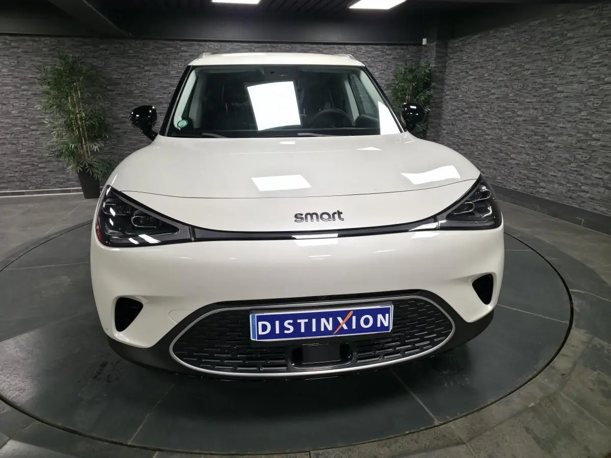 Vue avant d'une Smart #1 électrique blanche avec phares LED noirs et calandre basse distinctive.