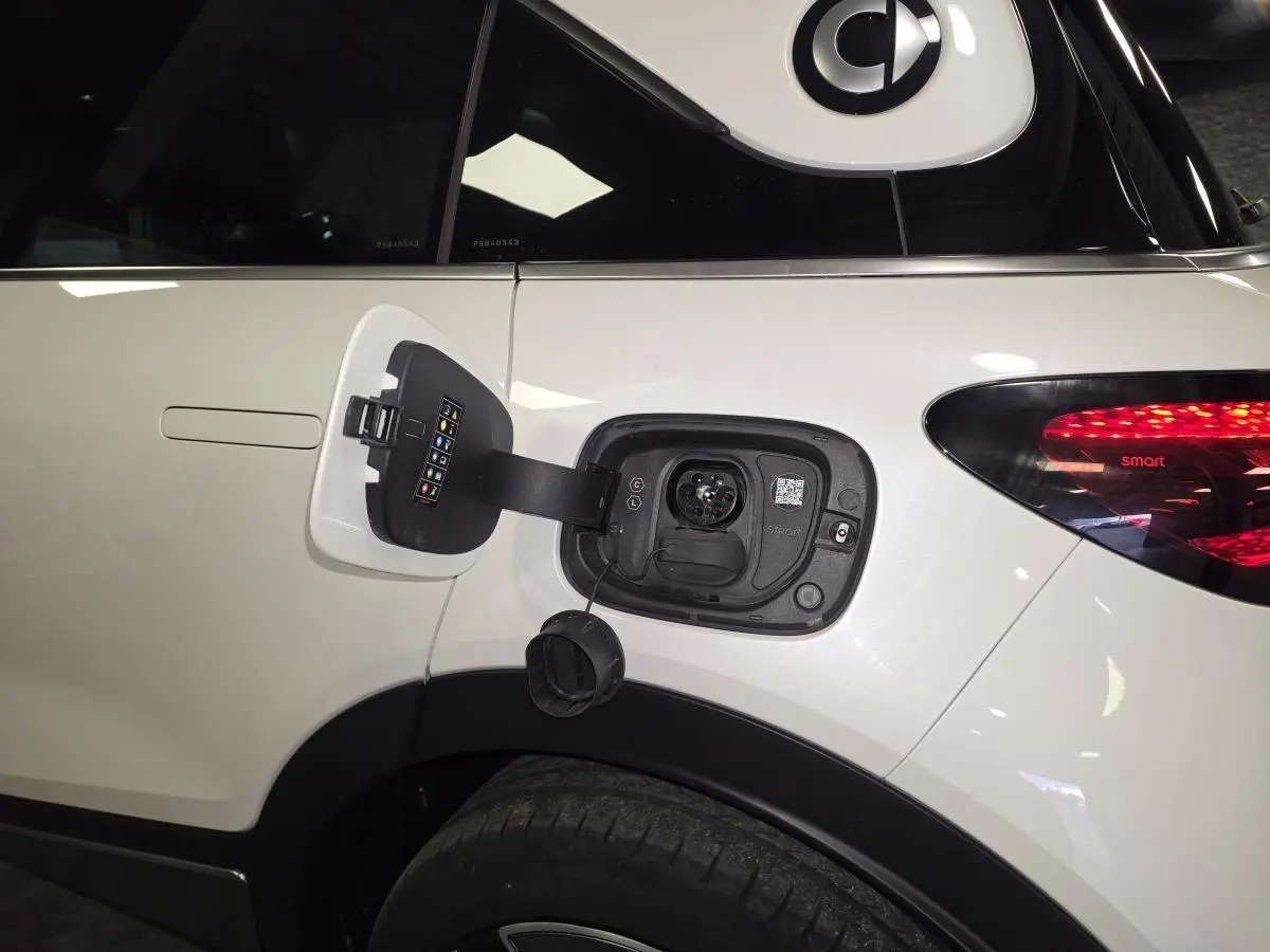 Vue latérale droite d'une Smart Electric blanche avec trappe de recharge électrique ouverte au-dessus de la roue arrière.