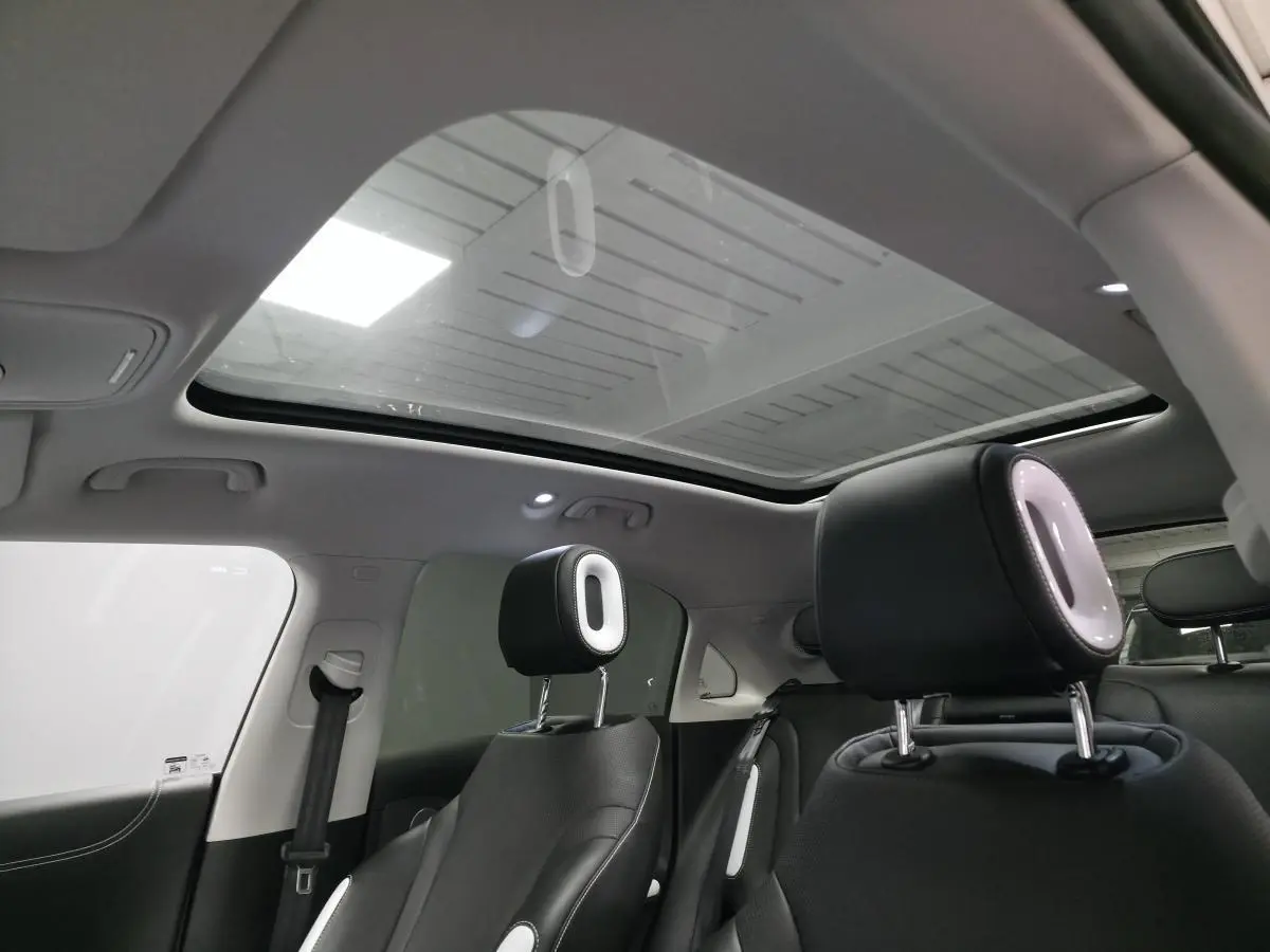 Intérieur de la Smart #1 électrique 2024, vue arrière montrant les sièges noirs avec appuie-têtes lumineux et toit panoramique en verre.