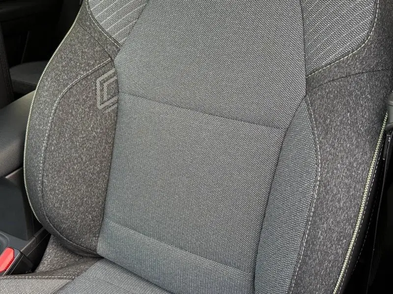 Gros plan sur le siège avant gris texturé du Renault Captur 2025, version hybride Rouge Flamme, avec surpiqûres apparentes.