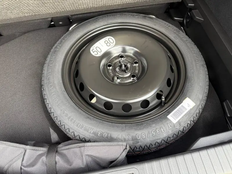 Pneu de secours noir dans le coffre d'un Renault Captur 2025 rouge flamme, vue plongeante sur la roue de secours.