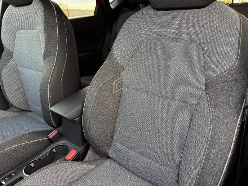 Gros plan sur les sièges avant en tissu gris du Renault Captur 2025, version hybride, avec surpiqûres contrastantes.