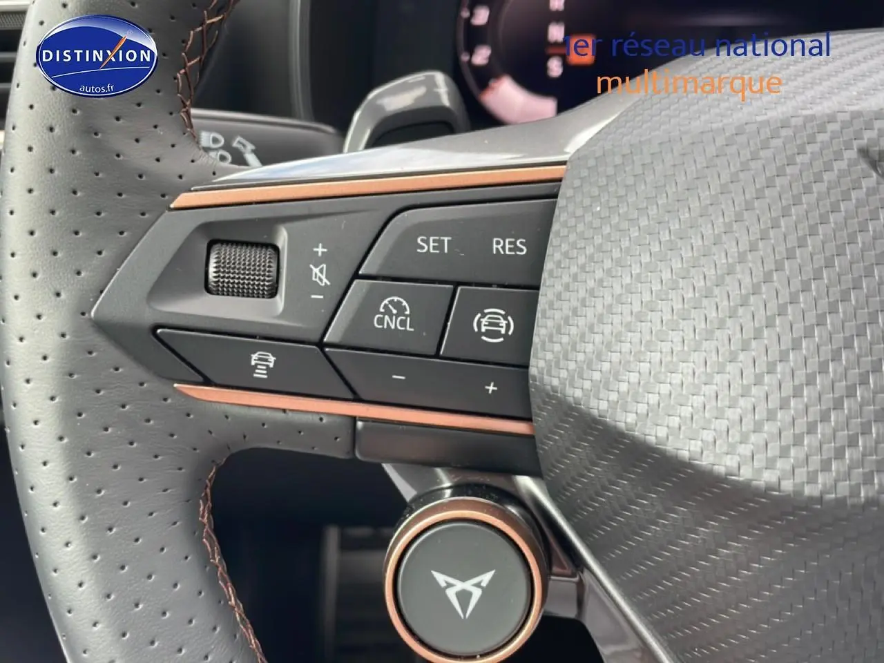 Gros plan sur le volant cuir perforé avec commandes multifonctions et logo CUPRA au centre, intérieur noir et cuivre.