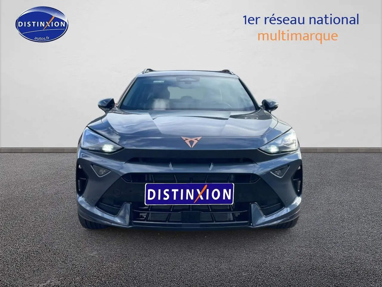 Vue frontale d'un CUPRA Formentor gris magnétique 2026 avec phares allumés et logo cuivré distinctif.
