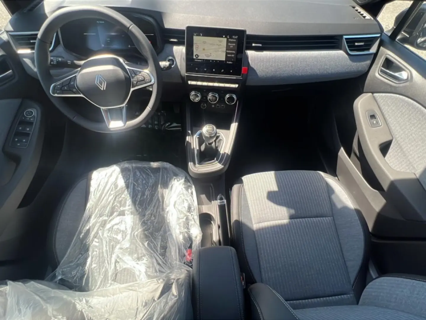 Vue intérieure avant de la Renault Clio V noire, montrant le volant multifonction et la console centrale avec écran tactile.