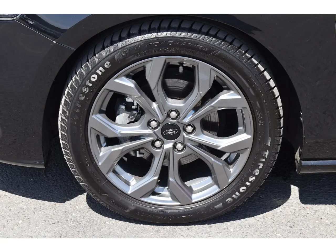 Gros plan sur la roue avant gauche de la Ford Focus SW 2025 Agate Black avec jante alliage grise et pneu Firestone.