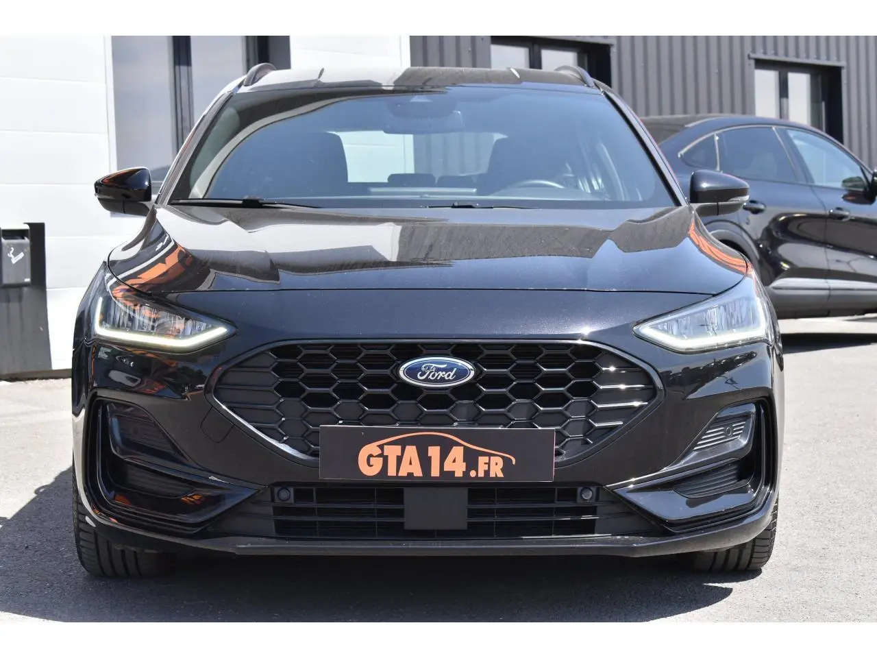 Vue avant d'une Ford Focus SW 2025 Agate Black Metallic avec calandre hexagonale et phares LED allumés.
