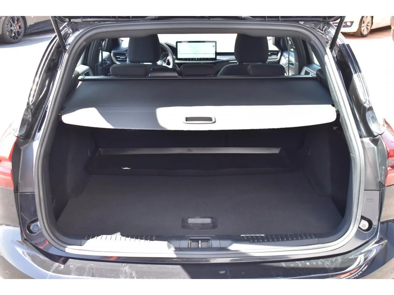 Vue arrière du coffre ouvert de la Ford Focus SW Agate Black Metallic, intérieur noir avec tablette cache-bagages déployée.
