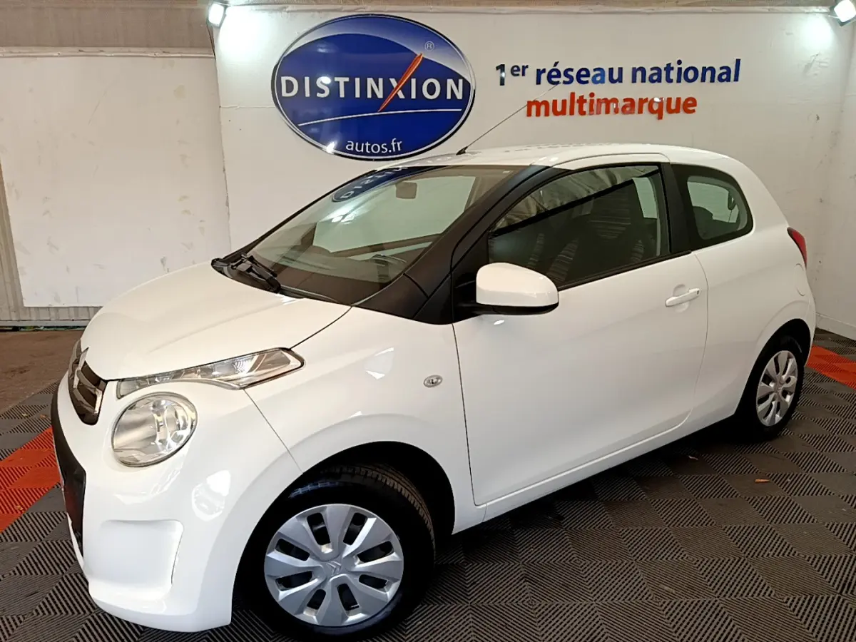 Citroën C1 blanc vue 3/4 avant droit en intérieur, avec jantes acier et rétroviseurs blancs.